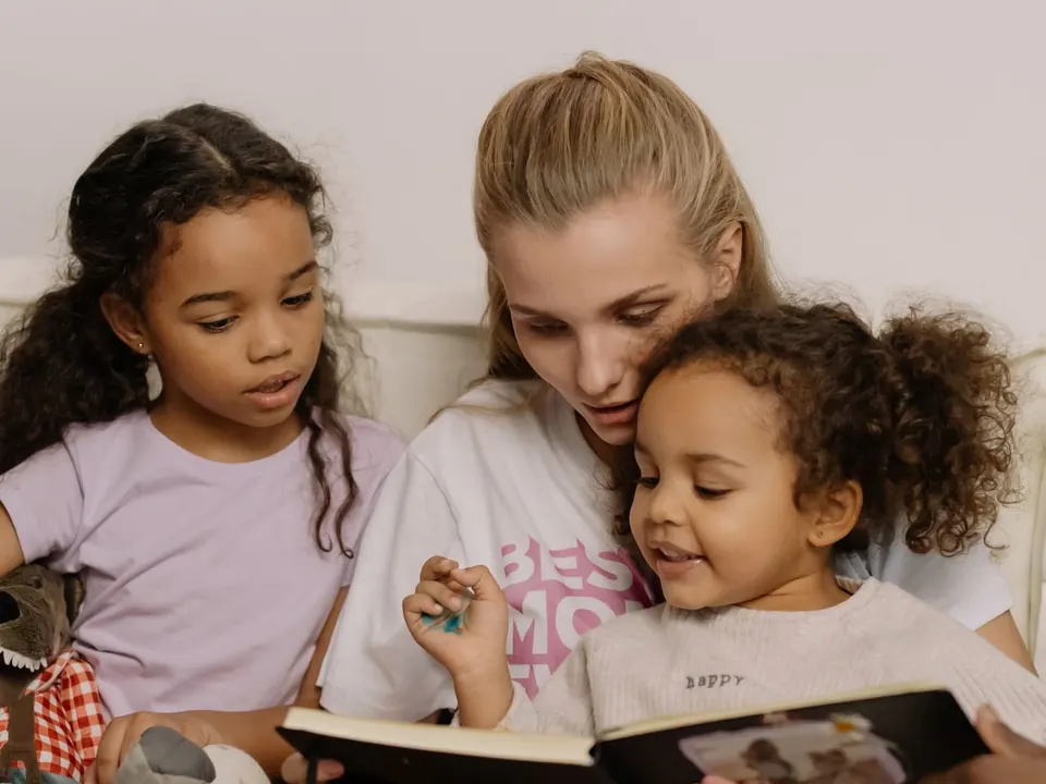 A mother reading a picture book with two young girls, one pointing at the page